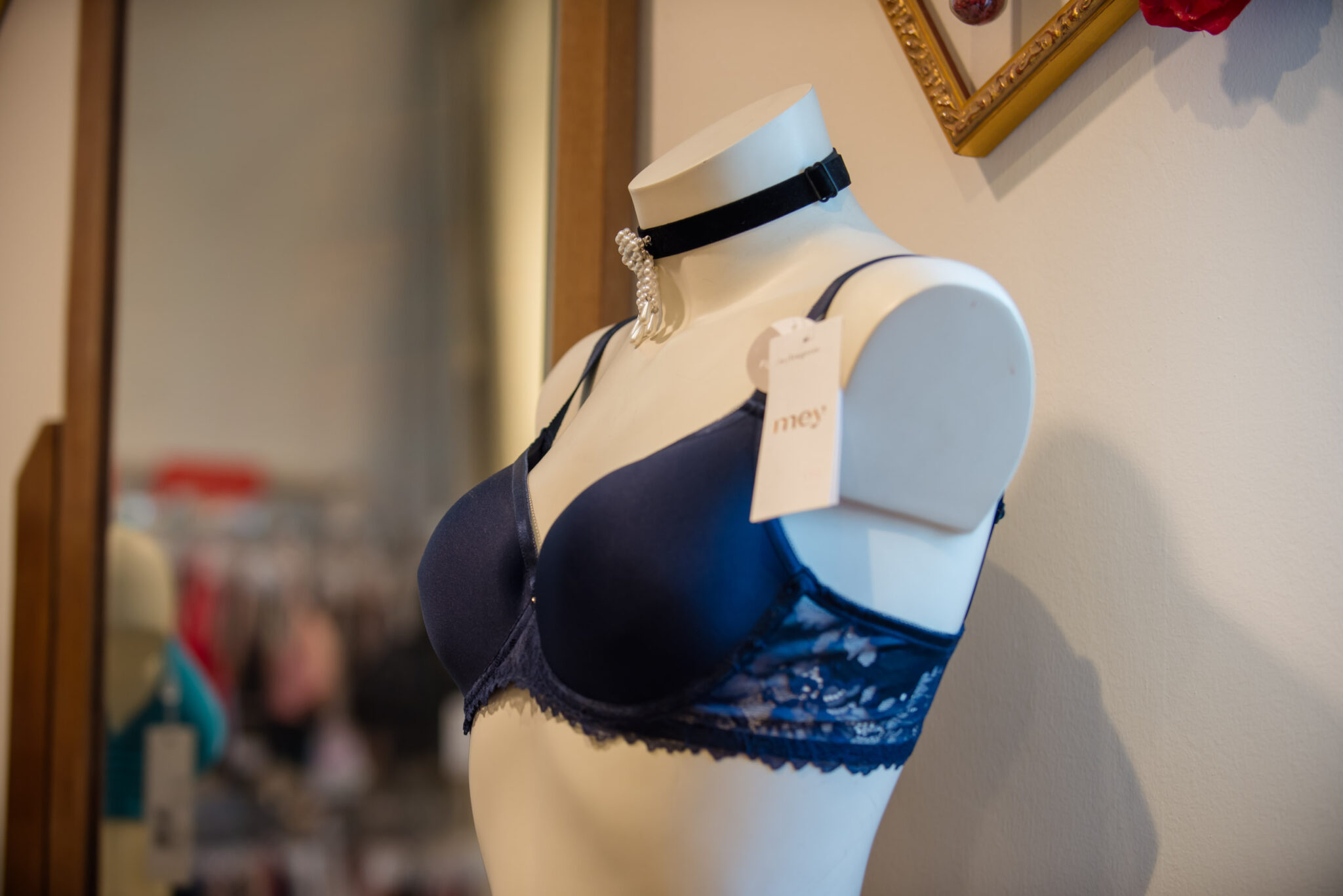 Dunkelblauer Spitzen-BH von Mey auf einem Ausstellungsmannequin in einem Obermaier Moden Laden, mit schwarzem Halsband und Perlen-Schmuck am Hals; Tag an der BH-Trägerseite sichtbar.